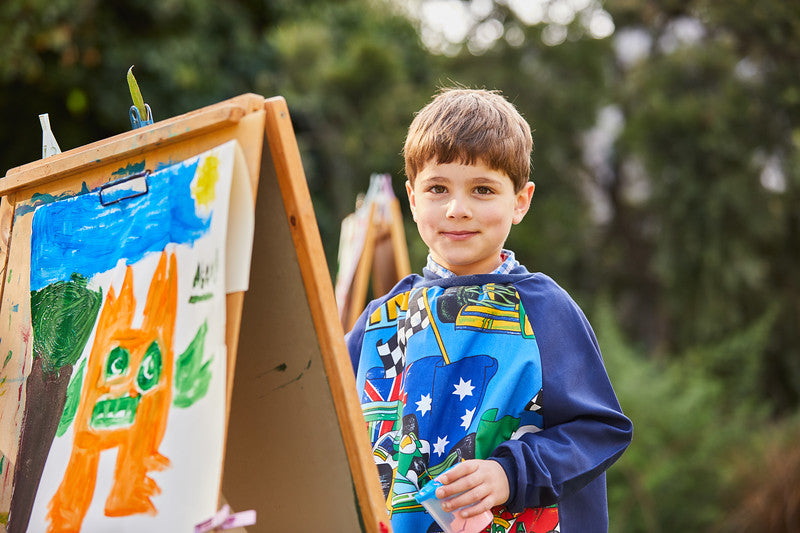 boy wearing racing car art smock at a painting easel