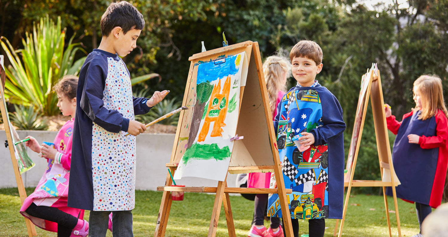 children painting at easels wearing art smocks